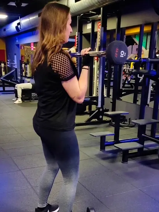 Clienta entrenando con barra en el gimnasio